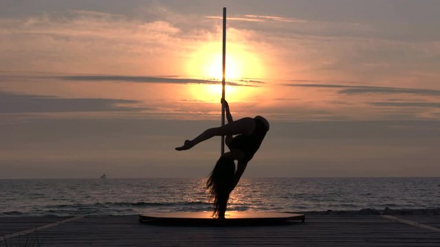 Fitness pole dance performance on the beach at sunset silhouette of fit girl poledancer against the setting sun during pole dancing exercise long shot part_S8