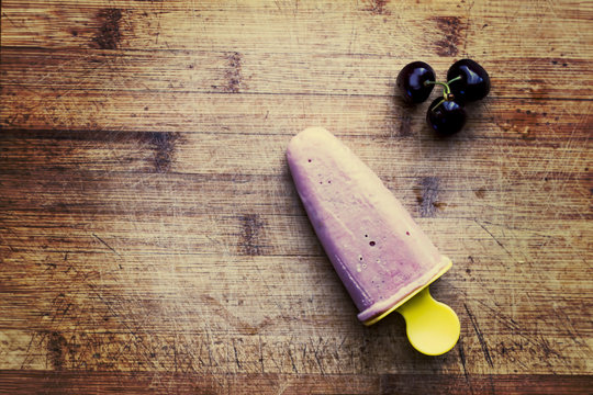 Homemade fresh cherry popsicle with berries on wooden cutting board. Toned image. Top view. Summer food concept.