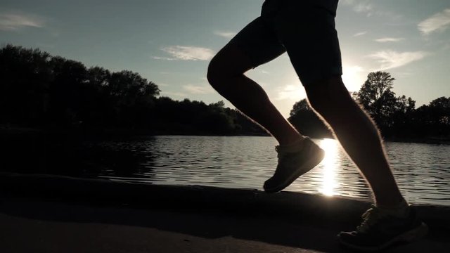 Super slow motion steadicam clip of sunset park runner on pond bank. Bleached
