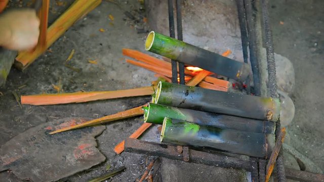 FullHD video - Local artist chopping kindling with a machete and adding it to a fire under a row of short bamboo tubes, drying them for use as a craft medium.