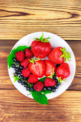 Mix of fresh, ripe berries in plate on wooden background.
