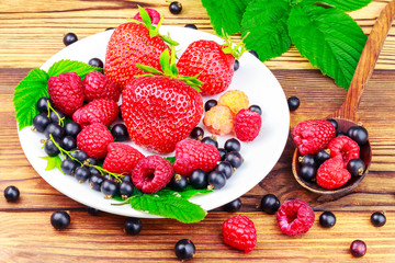 Mix of fresh, ripe berries in plate and spoon on wooden background. © O.Farion