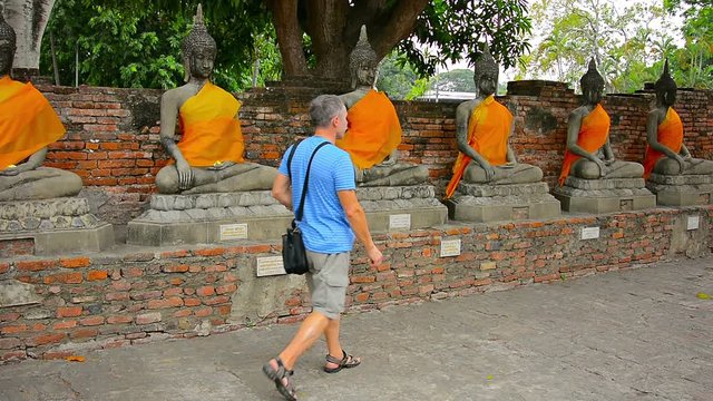 Video 1920X1080 - Tourist in casual clothes, strolls in front of a row of ancient, stone Buddha sculptures on a brick platform at Wat Yai Chai Mongkol in Thailand.