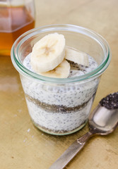 Organic yoghurt, sliced banana, chia seeds, served in a clean glass glass cup.