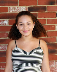 Pretty, Ethnic, Teenage Girl Smiling Against Brick Wall