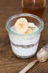 Organic yoghurt, sliced banana, chia seeds, served in a clean glass glass cup.