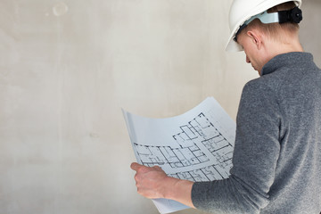 Naklejka premium An engineer in white safety helmet examining blueprints on a construction site