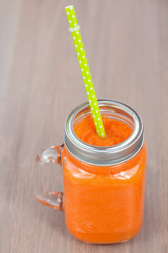 Healthy carrot smoothie in a jar with tube on wooden background. Shallow dof