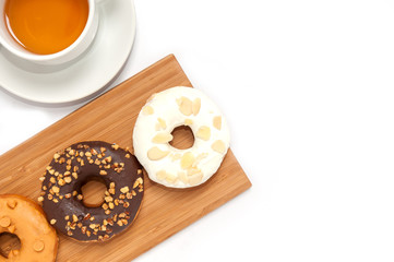Delicious donuts with icing and tae in wood plate isolated on white