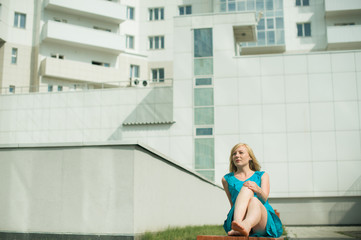 young blond woman sitting on a bench in the courtyard stretching her legs