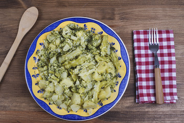 Cauliflower on a plate with patterned blue and yellow with a fork with wooden handle and a napkin white and red boxes on wooden table