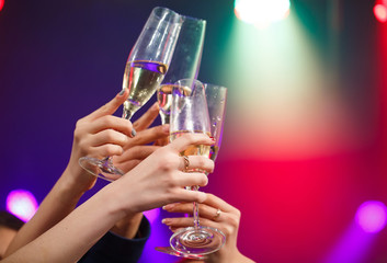 Clinking glasses of champagne in hands on bright lights backgrou