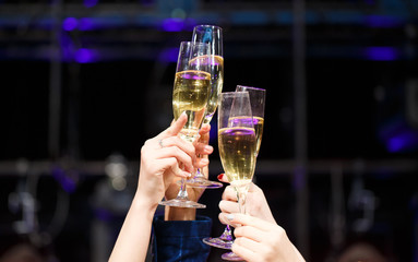 Clinking glasses of champagne in hands on bright lights backgrou