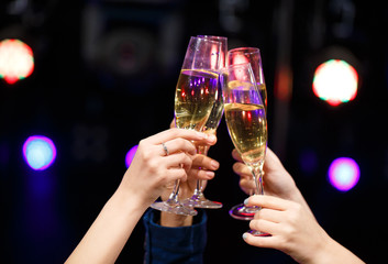 Clinking glasses of champagne in hands on bright lights backgrou