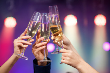 Clinking glasses of champagne in hands on bright lights backgrou