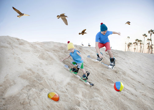 Two boys sandboarding on beach sand dunes, California, USA