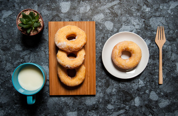 Delicious donuts with icing and cup of milk in plate on black marble table.