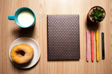 Office wood desk table with book,  supplies, donut and milk cup. Top view, Flat lay.