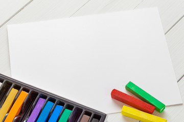 Naklejka premium Watercolor pastel crayons and white paper sheet of sketchbook on
