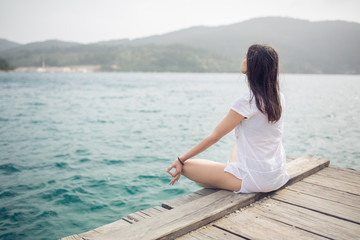 Fototapeta na wymiar Yoga and meditation concept.Woman meditating in sitting yoga position on pier.Woman alone practicing mindfulness meditation to clear her mind.Zen,meditation,peace concept