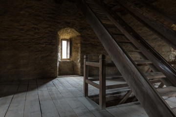 Fototapeta na wymiar Dark room with stone walls window and wooden staircase