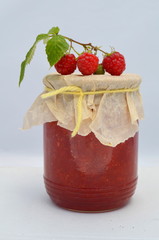 Банка малинового варенья на белом фоне и свежие ягоды малины рядом 