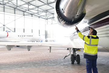 Flugzeugmechaniker kontrolliert Triebwerk eines Flugzeuges im Hangar // aircraft mechanic...