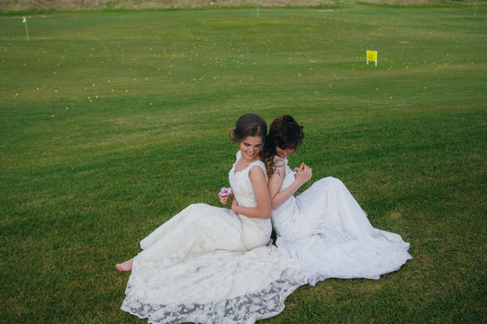 Two beautiful brides  sitting back to back on the green field of the golf club