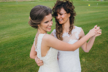 Two beautiful brides dancing  on the green field of the golf club