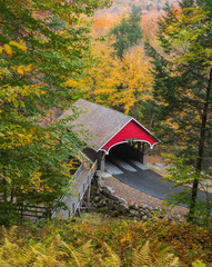New Hampshire Covered Bridge - The red covered wooden bridge across the Pemigewassett River in the White Mountains of New Hampshire stands out aginst colorful autumn foliage.