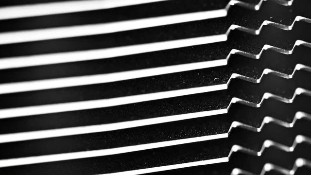 Video FullHD (1920x1080) - Light reflects off the fin points of an electronic heat sink, with deep shadow and black spaces between. Jagged steel teeth are perfectly aligned to the right of the frame.