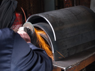 A man in a workshop using an industrial metal grinder to grind down stainless steel, creating vibrant orange sparks - obrazy, fototapety, plakaty