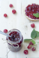 Himbeerkonfitüre im Glas mit Brötchen auf dem Frühstückstisc