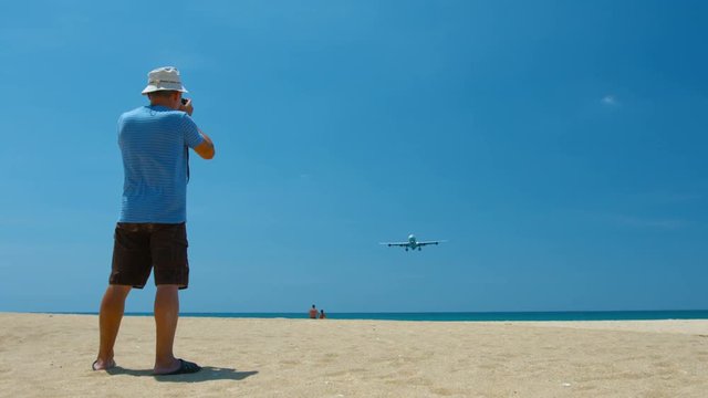 Video 3840x2160 - Photographer shooting a large, commercial airliner as it cruises low over a beach on final landing approach to Phuket International Airport in Thailand.