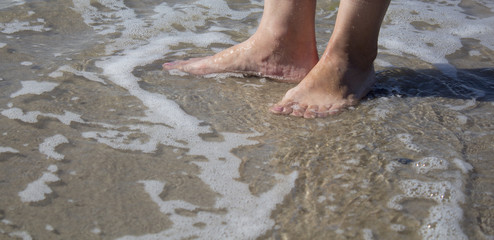 Sea foam, waves and naked feet on a sand beach. Holidays, relax