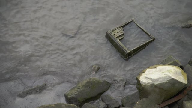 Discarded computer case on a riverbank covered in grime and algae.