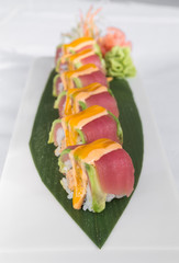 Fresh tuna sushi rolls, with wasabi and ginger sauce, served on a green leaf plate.