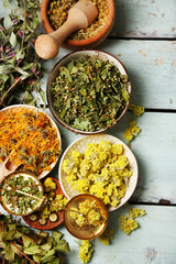 Assortment of dry medicinal herbs in bowls on wooden background top view