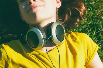 girl lying in summer grass with headphones listening to music