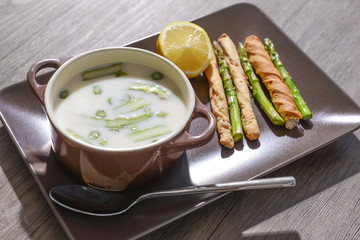 Asparagus soup with lemon and bread sticks on wooden table