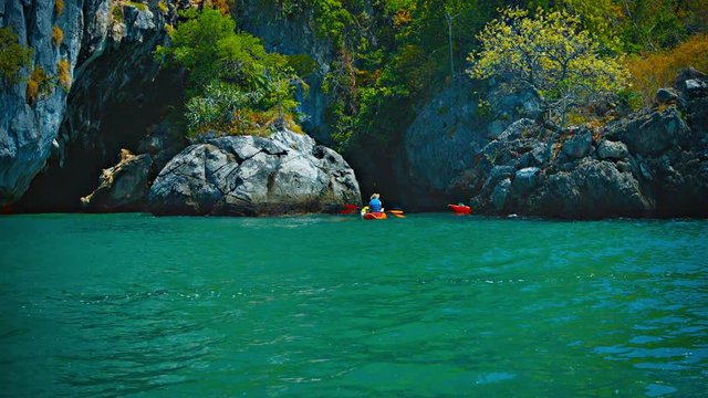 Video 1080p - Kayaking tourists paddle around an enormous boulder in a rocky inlet along the coastline of a tropical island in Southeast Asia.