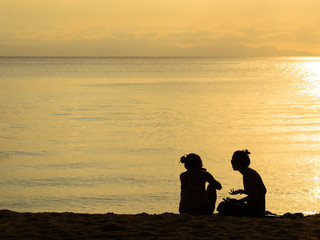 Fototapeta na wymiar Silhouette of two women together sitting and talking on beach.