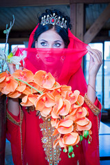 Portrait of a beautiful woman in oriental dress. Grace and beauty. Young girl in a red dress expensive Arabic covers her face with a handkerchief.