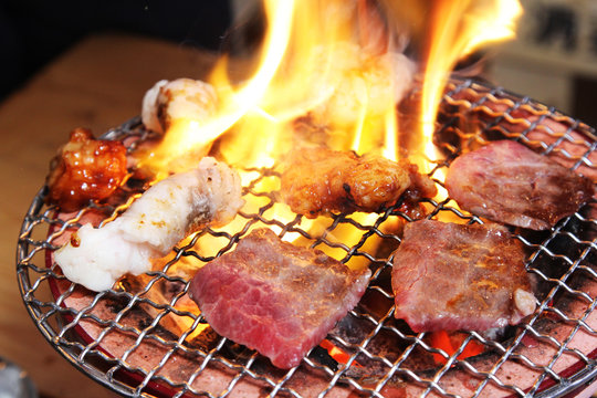 Japanese BBQ meat sizzling on grill with flames and smoke