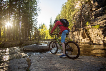 Obraz premium Cyclist with a backpack traveling on a mountain river at sunset