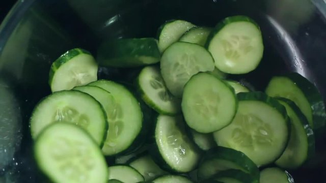 Close up of slices of cucumber falling into glass bowl