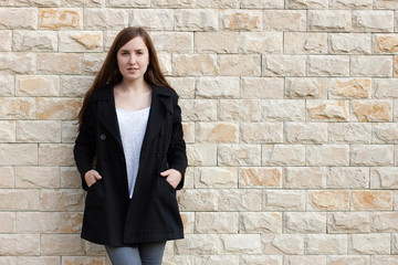 Fototapeta na wymiar Girl in black coat near brick wall