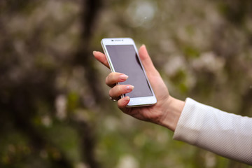 woman holds a smartphone telephone over blossoming spring tree background, soft focus, close up