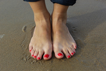Pies de mujer con uñas pintadas de rojo sobre la arena de la playa.