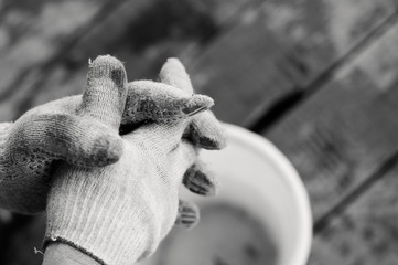 Male hand in a dirty working gloves, close-up, wood background, black-and-white image.